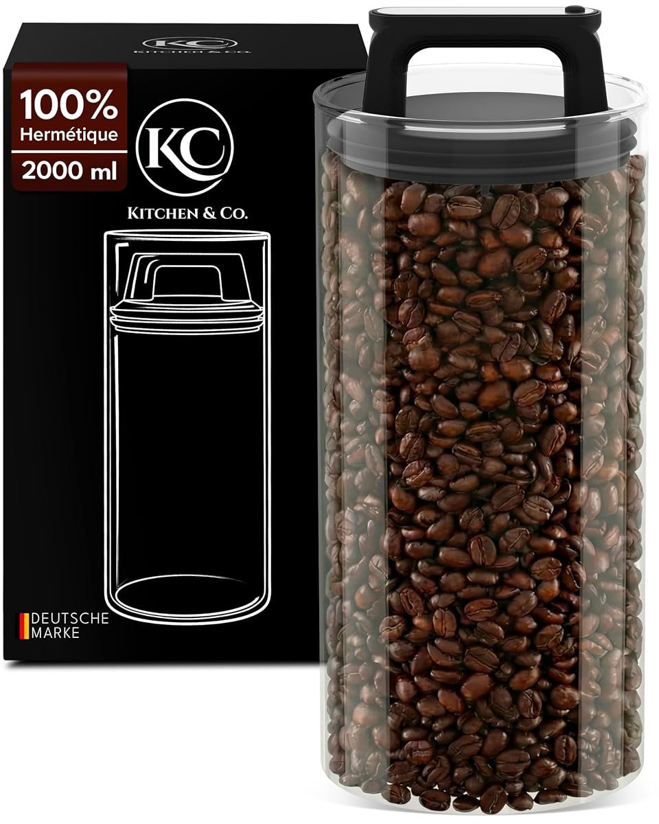 Boîte à café ronde en verre transparent avec couvercle sous vide et grains visibles sur un plan de travail en bois.