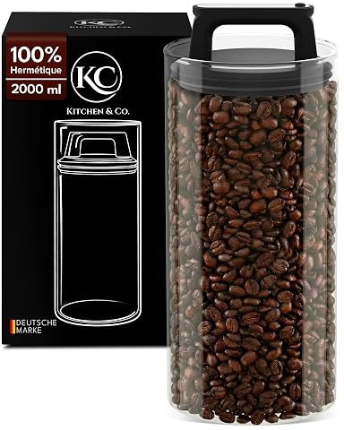 Boîte à café ronde en verre transparent avec couvercle sous vide et grains visibles sur un plan de travail en bois.